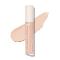 Tube of high coverage concealer in salmon beige shade with creamy swatch background on white surface