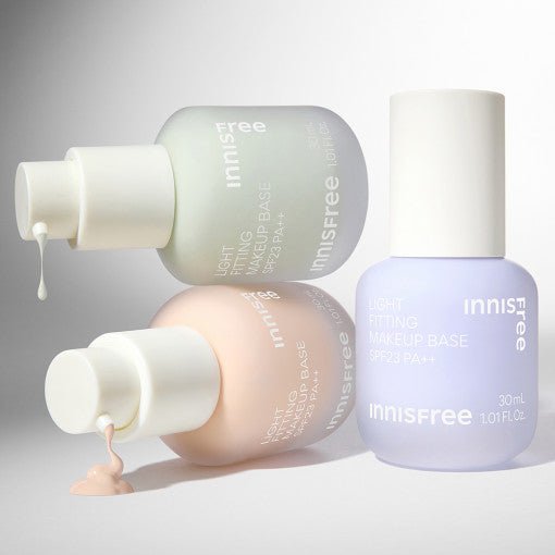 Three pastel bottles of lightweight makeup base with creams dripping from pump tops on a neutral background