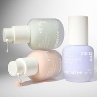 Three pastel-toned bottles of makeup base with droppers showing lightweight cream and liquid textures on a plain background