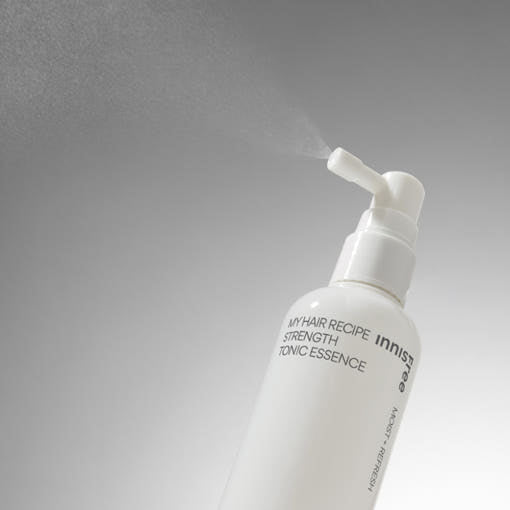 White spray bottle of hair tonic essence emitting fine mist against a neutral gradient background