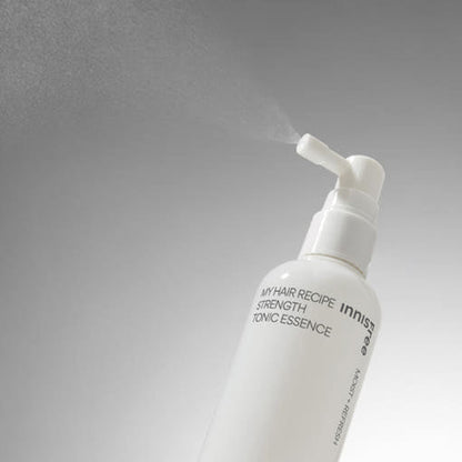White spray bottle of hair tonic essence emitting fine mist against a neutral gradient background