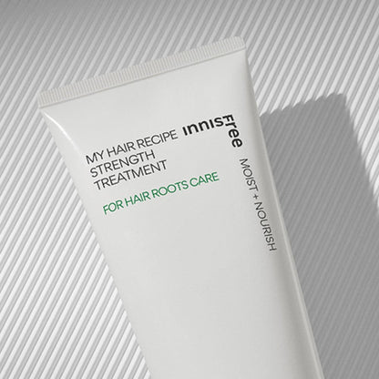 White treatment tube with black and green text highlighting hair root care and nourishing benefits on textured background