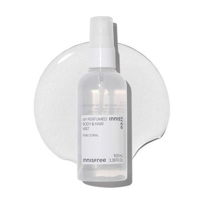 Clear spray bottle of refreshing body and hair mist with subtle pink coral label on a white textured background
