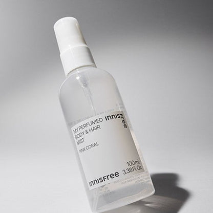 Clear spray bottle of perfumed body and hair mist with minimalist white label on gray background