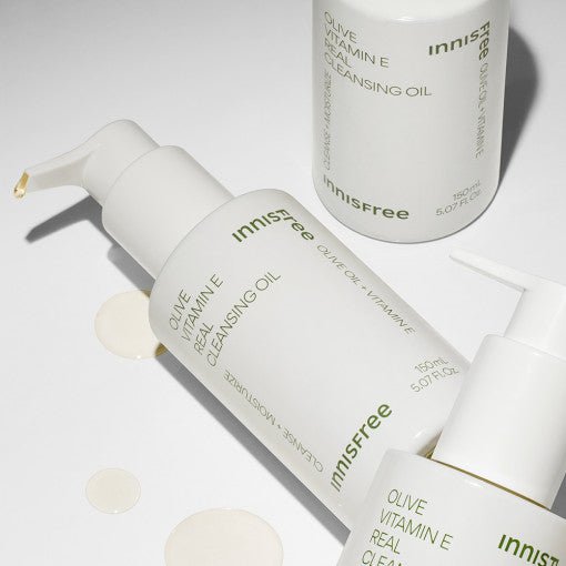 White pump bottles of olive vitamin E cleansing oil with moisturizing formula on a light neutral background