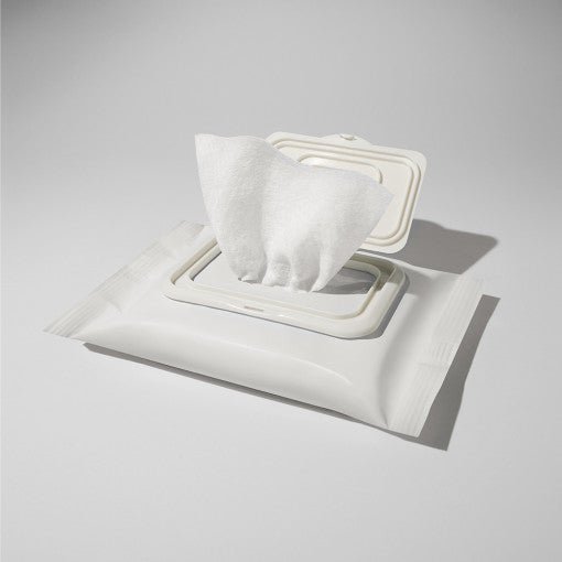 White resealable pack of cleansing tissues with one tissue partially pulled out on light gray background