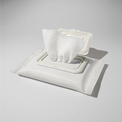 White resealable pack of cleansing tissues with one tissue partially pulled out on light gray background