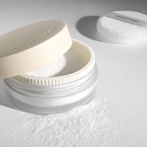Translucent loose powder container with soft beige lid and white puff applicator on light surface