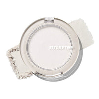 Compact of sheer highlighter powder with soft shimmer and natural glow beside crushed product on white surface