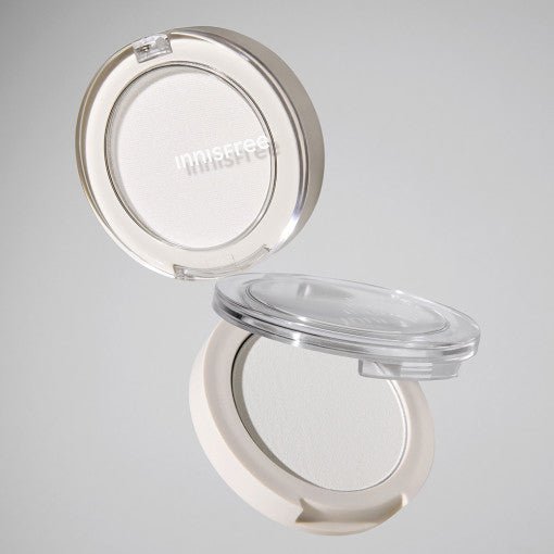 Open compact of pale beige highlighter powder with sheer natural glow in minimalist packaging