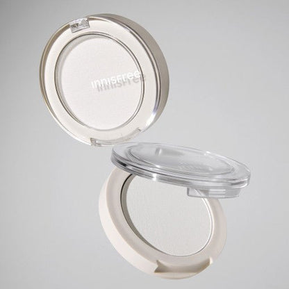 Open compact of pale beige highlighter powder with sheer natural glow in minimalist packaging