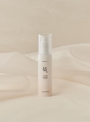 Minimalist beige bottle of ginseng sun serum with a clear pump cap for lightweight UV protection on soft fabric background