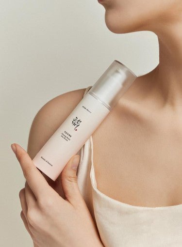 Hand holding a frosted bottle of ginseng sun serum with SPF50+ PA++++ against bare shoulder and light background