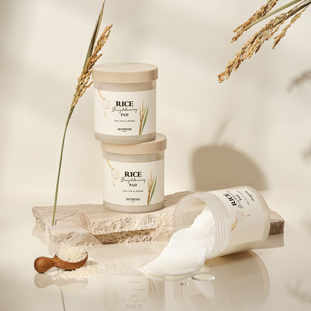 Stacked beige jars of brightening rice pads with scattered pads spilling from one jar on a textured stone block