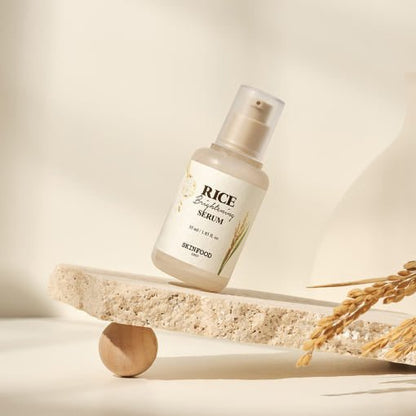 Minimalist frosted bottle of brightening serum with rice grain illustration balanced on textured stone slab with rice stalks nearby