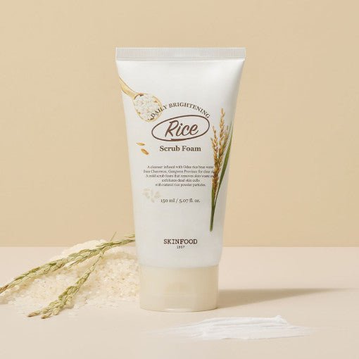 Tube of brightening rice scrub foam with gentle exfoliation benefits on beige background with rice grains and stalks