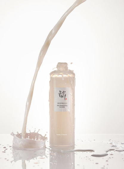 Creamy liquid flowing into an open translucent bottle of Glow Replenishing Rice Milk with splash on white surface