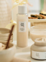 Minimalist translucent bottle of glow replenishing rice milk with a white cap and soft beige background setting