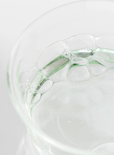 Clear pale green toner liquid with bubbles in a transparent glass container for gentle exfoliation skincare