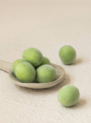 Fresh green plums arranged on a wooden spoon with a minimalist neutral background for natural skincare concept