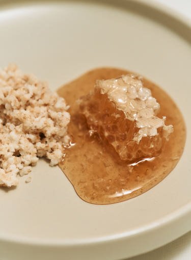 Close-up of ground rice grains and honeycomb piece with golden honey on a smooth beige surface promoting radiant skin benefits