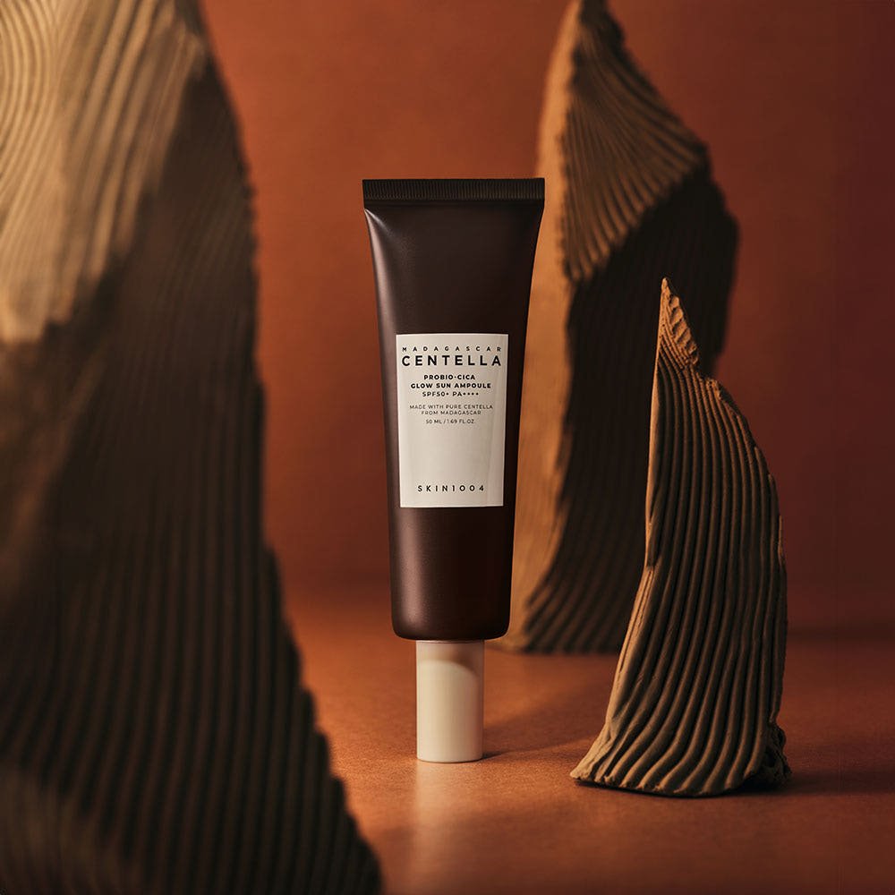 Dark brown tube of Centella Probio-Cica Glow Sun Ampoule with white cap on warm brown artistic background