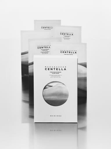 Set of five white skincare mask packets with minimalist text highlighting brightening tone effect on gray background