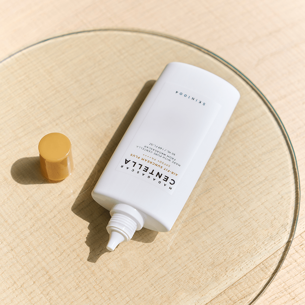 White suncream tube with a mustard yellow cap removed, showing a pointed nozzle on a textured surface in natural light