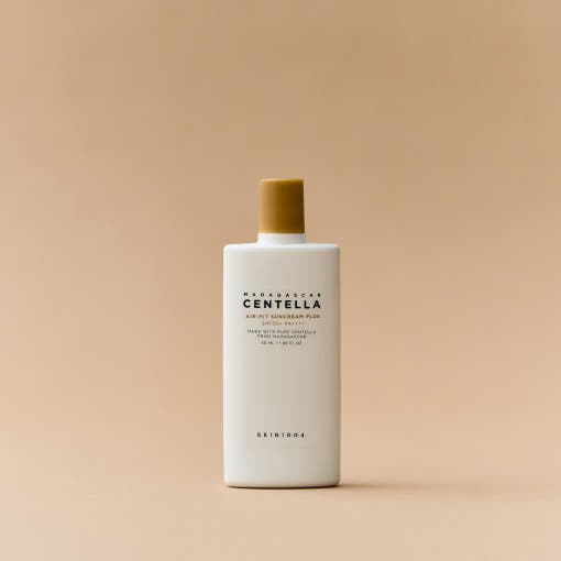 Minimalist white bottle of Centella air-fit suncream with mustard yellow cap on neutral beige background