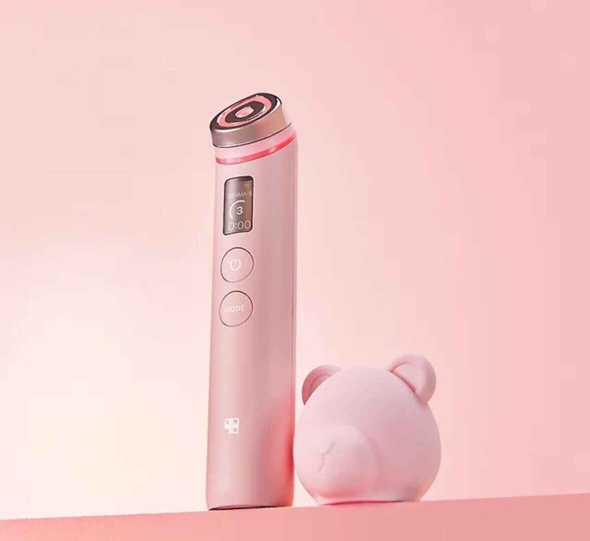 medicube AGE-R Booster Pro #Pink device standing next to round bear-shaped pink accessory on soft pink background