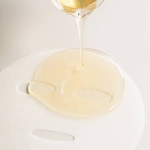 Clear gel serum being poured onto white sheet mask with smooth texture, highlighting intense hydration benefits