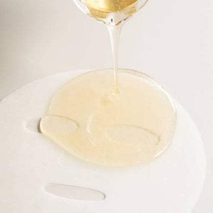 Clear gel serum being poured onto white sheet mask with smooth texture, highlighting intense hydration benefits