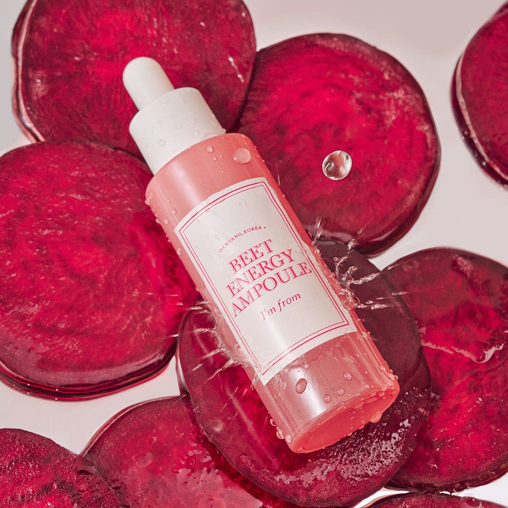 Dropper bottle of hydrating pink ampoule resting on vibrant sliced beetroot pieces with water droplets