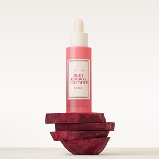 Pink ampoule bottle with white dropper cap standing on stacked beetroot slices on white background