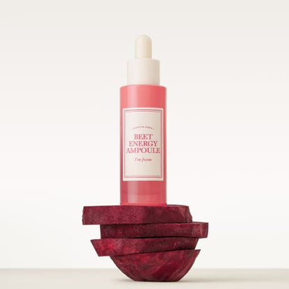 Pink glass dropper bottle of hydrating ampoule balanced on stacked beetroot slices against a soft background