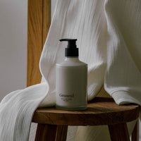 Minimalist glass pump bottle of creamy lotion placed on wooden stool with soft white fabric backdrop