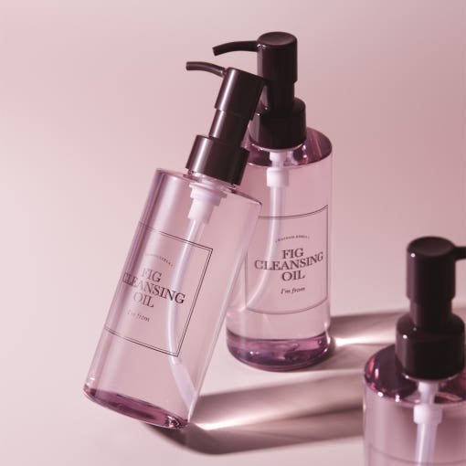 Clear pump bottles of gentle cleansing oil with soft pink tint displayed on pale pink surface