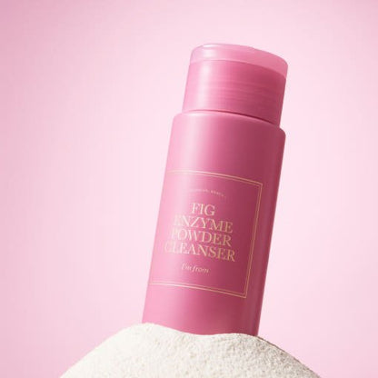 Pink cylindrical bottle of enzyme powder cleanser partially embedded in white powder with soft pink background