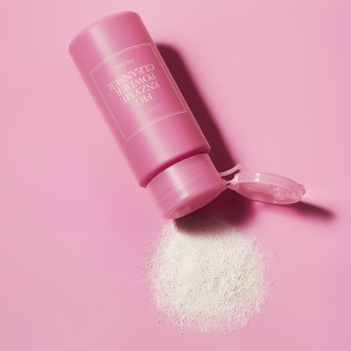 Pink container of exfoliating enzyme powder cleanser spilling fine white powder on a pastel pink background