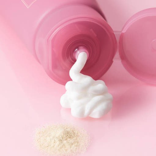 Soft white foam dispensing from pink cleanser tube with fine powder on smooth pink surface