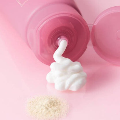 Soft white foam dispensing from pink cleanser tube with fine powder on smooth pink surface