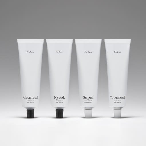 Four minimalist white tubes of hand cream with black and white caps arranged in a row on a neutral background