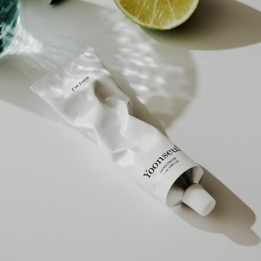 White crumpled tube of hand cream on white surface with light reflections and halved lime in background