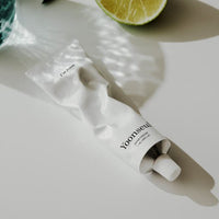 Squeezed white tube of long-lasting hydrating hand cream casting soft shadow near lime slice on pale surface