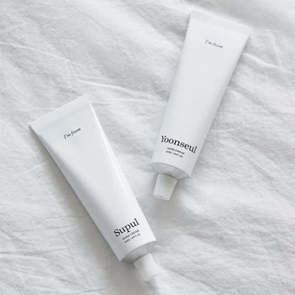 Two minimalist white tubes of hand cream labeled Supul and Yoonseul on soft white fabric background