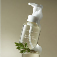 Clear pump bottle of soothing feminine wash with foamy lather and fresh green mugwort leaf on beige background