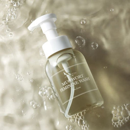 Clear pump bottle of soothing feminine wash with light amber liquid and water bubbles background
