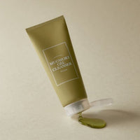 Olive green tube of gentle mugwort gel cleanser with clear green gel spilled on beige surface