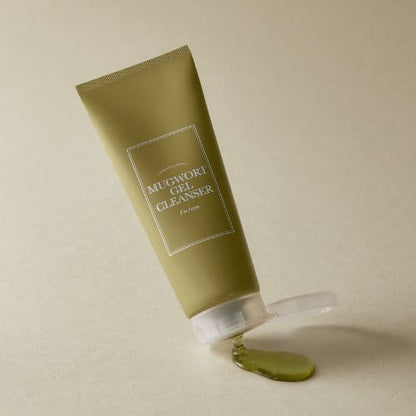 Matte olive-green tube of gentle cleansing gel cleanser with clear green gel spilled on beige surface background