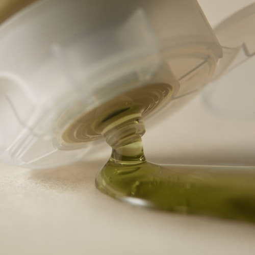 Light green gel cleanser dispensing from a clear squeeze bottle, highlighting gentle cleansing texture and color